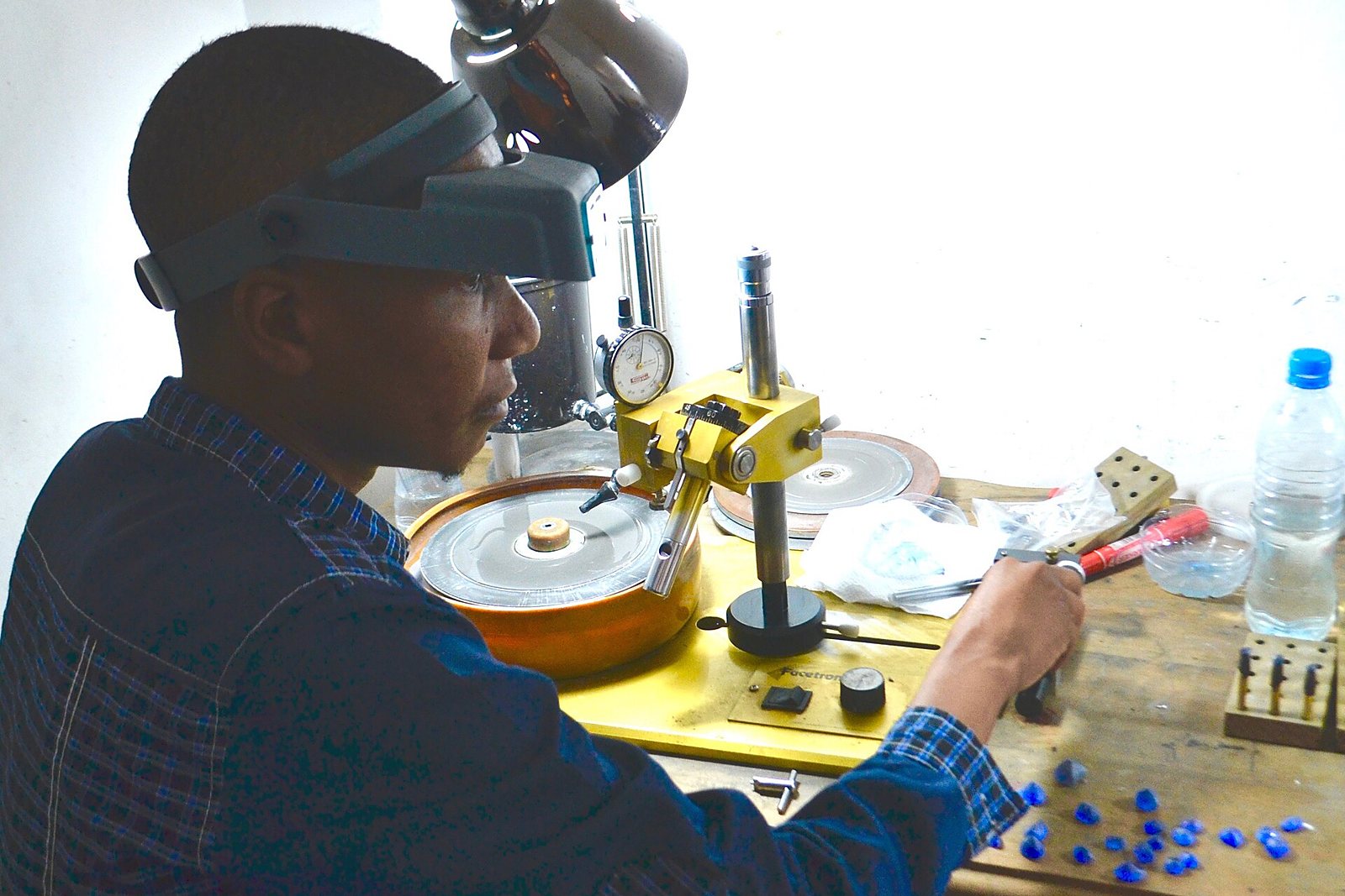 A gem cutter faceting a stone at his wheel