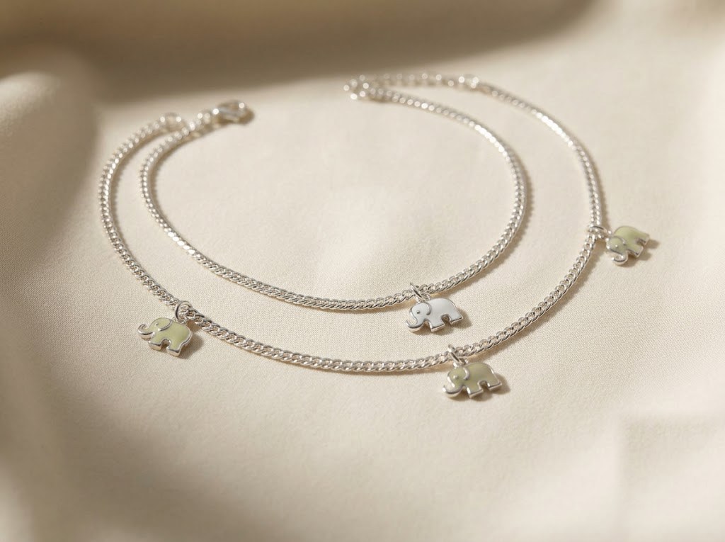 Pair of fine silver anklets with small enamelled elephant charms on cream silk