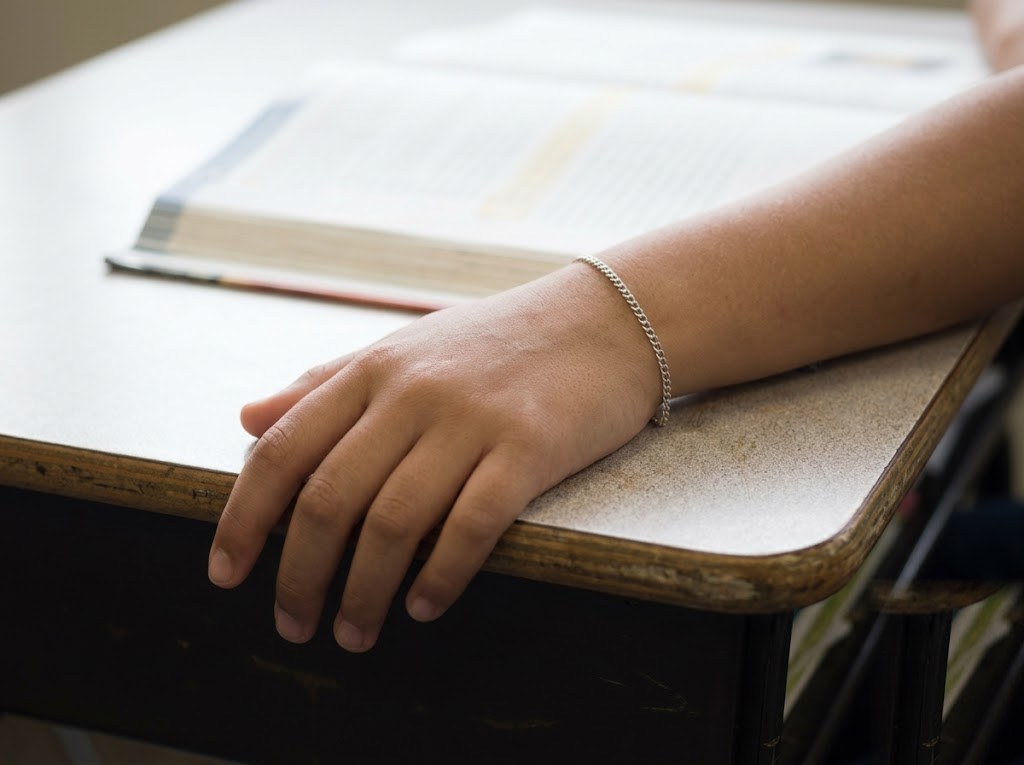 Child's hand on a school desk wearing a thin silver chain bracelet