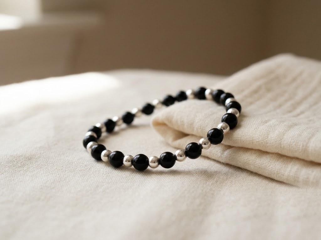 Silver nazariya bracelet with black beads resting on a cream muslin cloth